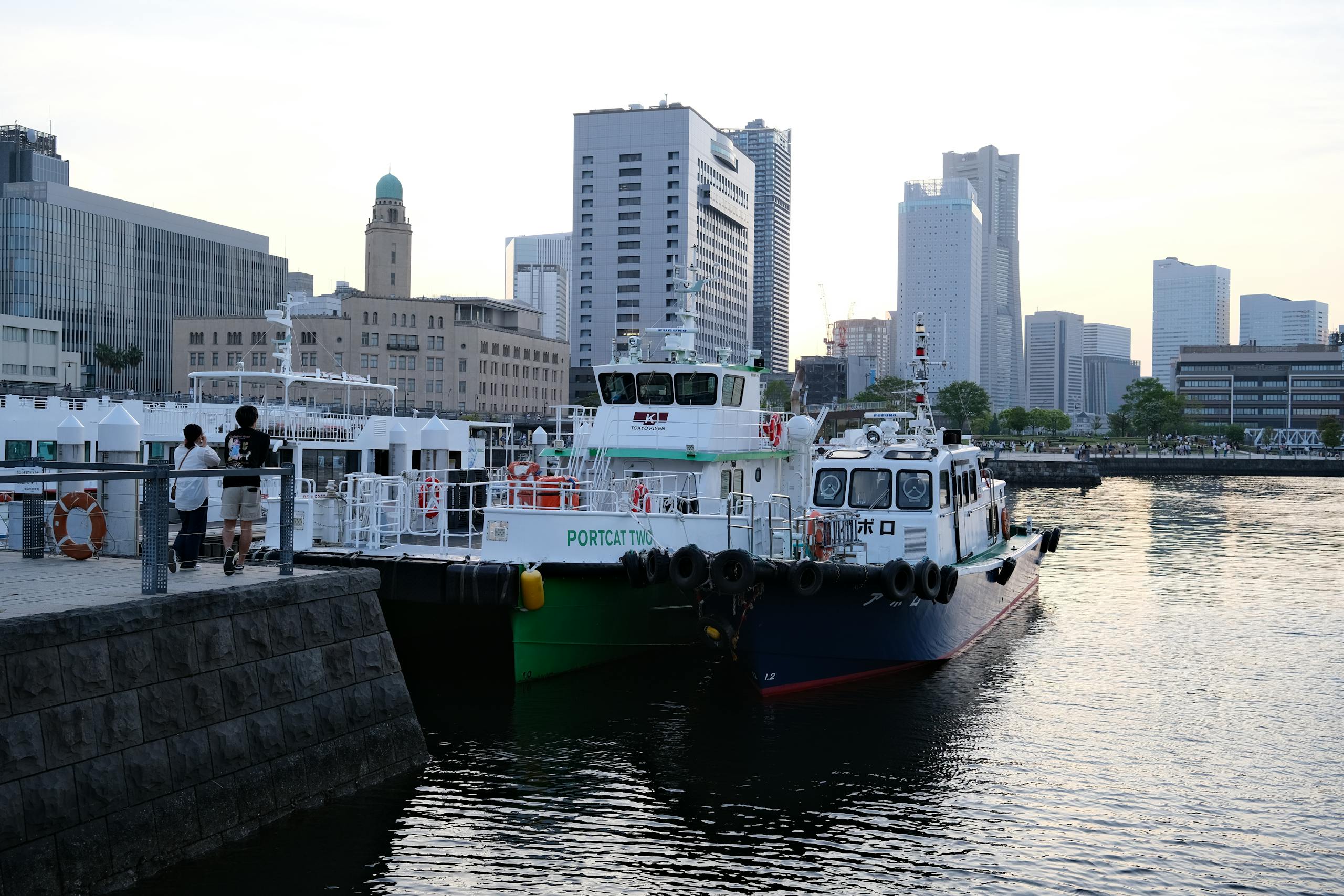 Capture the serene evening at Yokohama Harbor with boats moored against a backdrop of city skyscrapers.